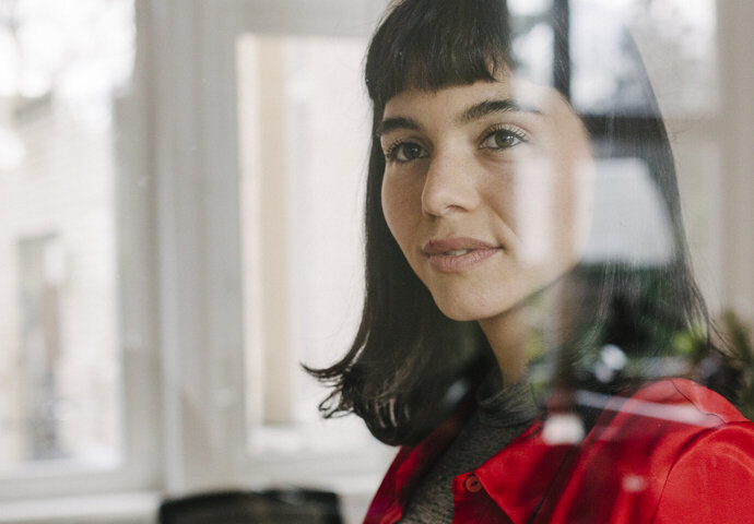 Junge Frau schaut mit einem zuversichtlichen Blick in die Zukunft aus dem Fenster.