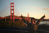 Frau steht vor Golden Gate Bridge und hät die Arme in die Höhe